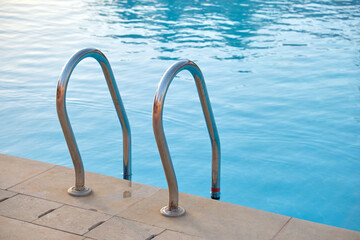 Obraz na płótnie Canvas Close up of swimming pool stainless steel handrail descending into tortoise clear pool water. Accessibility of recreational activities concept