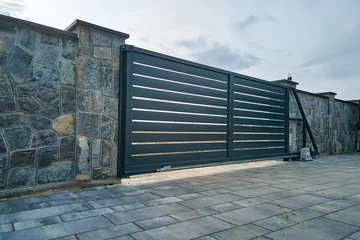 Fotobehang Wide automatic sliding gate with remote control installed in high stone fense wall. Security and protection concept © bilanol