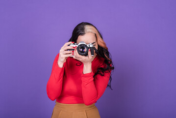 Attractive young lady taking a photo with her film camera over a violet background.