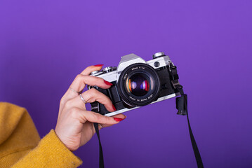 Close up of a female hand holding a film camera over a violet background.