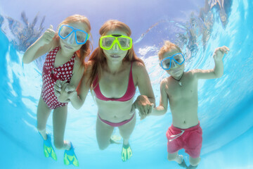 Happy people dive underwater with fun. Funny photo of mother, kids in snorkeling masks in aqua park...