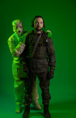soldier in studio on green background with medic or scientist a man in military uniform with a rifle or machine gun of a man in chemical protection put a syringe to his neck. chemical bacterial threat