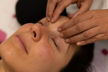 Fototapeta na wymiar Latina woman receiving a Shiroadhyanga massage on the face with specific pressure points