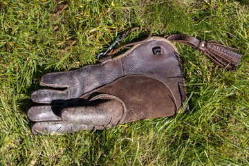 One leather glove with a long cuff for working with birds of prey, lying in green grass.
