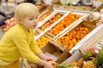 Cute toddler boy in a food store or a supermarket choosing fresh organic pineapple. Healthy lifestyle for kids