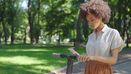 African American woman renting electric scooter via smartphone app in park