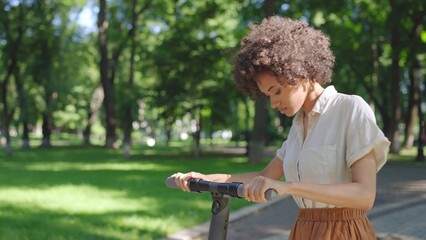 Young biracial woman learning to ride electric scooter in park, first experience - Powered by Adobe