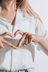 romantic young woman in shirt making a heart gesture with her fingers in front of her chest showing her love and affection