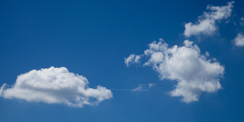 Le sillage d'un avion forme un trait d'union entre deux cumulus dans un ciel bleu