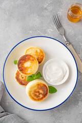 Cottage cheese pancakes, syrniki, ricotta fritters with honey and sour cream on a gray concrete background. Healthy and delicious breakfast. Top view, copy space.