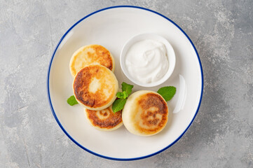 Cottage cheese pancakes, syrniki, ricotta fritters with honey and sour cream on a gray concrete background. Healthy and delicious breakfast. Top view, copy space.