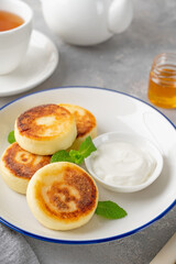 Cottage cheese pancakes, syrniki, ricotta fritters with honey and sour cream on a gray concrete background. Healthy and delicious breakfast. Top view, copy space.