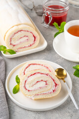 Sponge cake roll with strawberry jam and cream on a white plate on a gray background. Copy space.