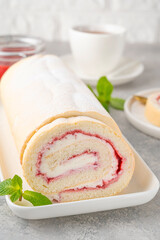 Sponge cake roll with strawberry jam and cream on a white plate on a gray background. Copy space.