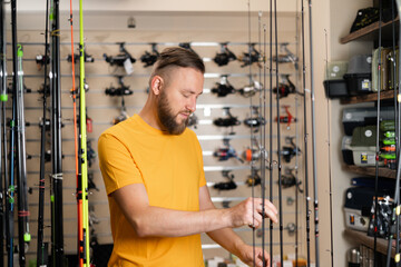 Millennial man chooses fishing rod in the sports shop