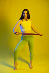 Fototapeta na wymiar Athletic girl in green leggings and a blue t-shirt does exercises for the buttocks with a resistance band. Fitness woman exercising. yellow background.