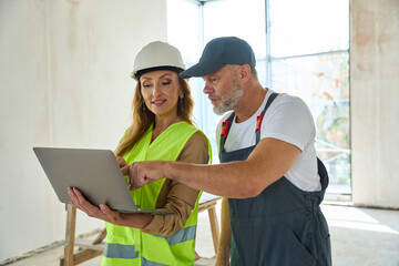 Gray-haired builder points finger at laptop held by sales manager