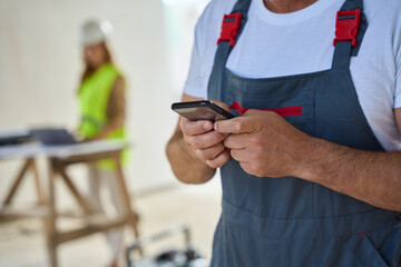 Cropped photo of construction worker typing message on phone