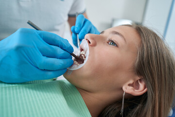 Professional pediatric dentist inspecting young patient teeth