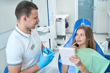 Fototapeta premium Teenage patient discussing dental problems with male doctor at consultation