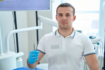 Professional male dentist showing diagnostic tools for oral cavity examination