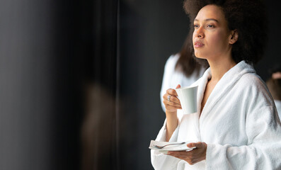 Beautiful black woman relaxing at luxury hotel spa wearing bathrobe and drinking coffee