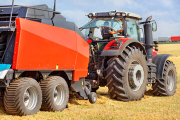 An agricultural tractor with a large trailer for harvesting wheat against the background of a harvested field.
