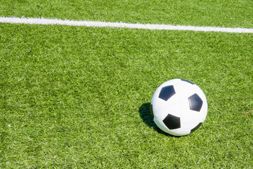 Fototapeta na wymiar Green artificial turf soccer field with white line, shadow from football goal net and soccer ball on sunny day outdoors. Top view. Football soccer sport background
