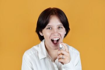 A modern teenage girl is smiling on orange background and holding a bottle of refreshing mouthwash,...