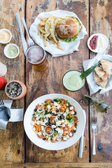 Burger with french fries and cheese salad, lettuce, tomato, olives, onion and cheese, with beer and fruit juice, on a wooden table.