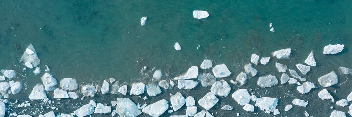 Top view of the white ice floes on the shore and in the blue sea water. Aerial view of melting ice...