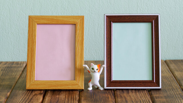 Two different blank empty frames for pictures or photos. Next to funny toy dancing cat from meme on wooden table. Fillable element of the interior of the children's room. Copy space.