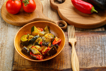 A plate of grilled vegetables next to tomatoes and eggplant and peppers on wooden boards next to a wooden fork.