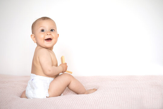A cute little girl in a white diaper sits on a pink knitted blanket. Lifestyle. Happy Childhood. Space for text