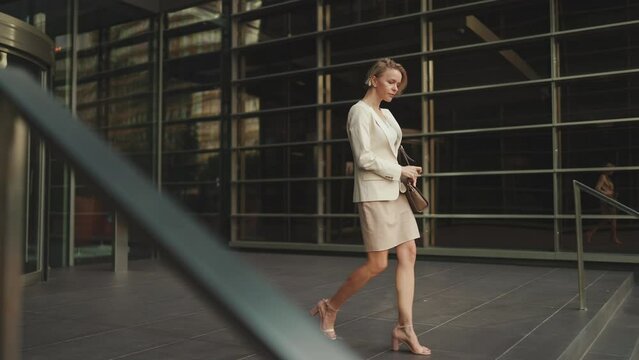Businesswoman with blond hair wearing beige suit leaving business center