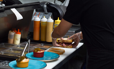 Restaurant kitchen employee working on preparing sandwich for customer food order