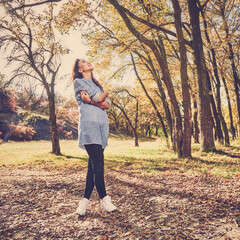 Young stylish girl having walk in autumn park on sunny day