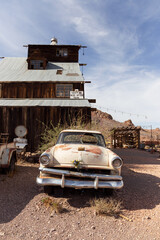 Album cover inspired rusted classic American vintage hotrod sits outside ghost town barn in front of sign that reads don't be here after dark