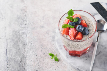 Chia strawberry pudding. Healthy vegan breakfast chia seeds pudding with fresh berries and mint in glass on gray concrete background. Concept of healthy eating, dieting, fitness menu. Selective focus.