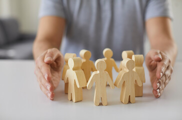 Social protection. Wooden figurines of people surrounded by man's hands symbolizing care for...