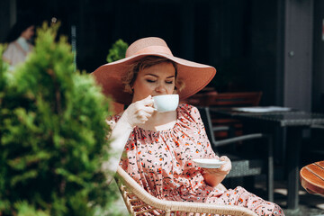 Outdoor fashion portrait of a stunning woman sitting in a cafe. I drink coffee and read an old book. a woman in a dress and a hat.