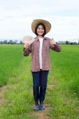 Front view of female farmer wear hat posing with banknotes smiling in a rice field.