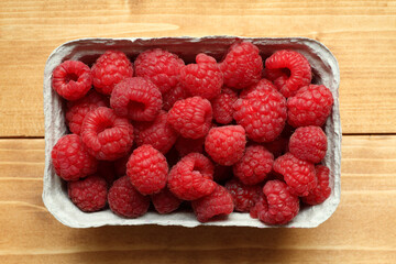Raspberries are in a cardboard box, which stands on a wooden table. View from above