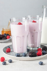 Smoothie from berries, natural yogurt and honey in two tall glasses on light gray background
