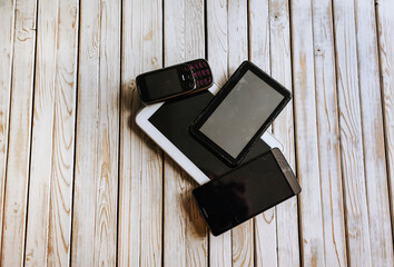 Old broken unnecessary gadgets, smartphones lie on a wooden background.