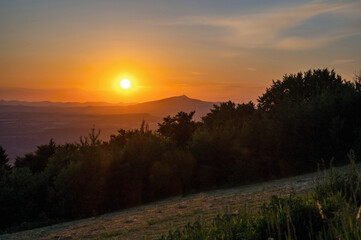 Sunset over mountains, forest and meadow, hill Jested on horizon, Czechia.