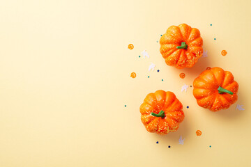 Halloween concept. Top view photo of orange pumpkins and confetti on isolated beige background with...