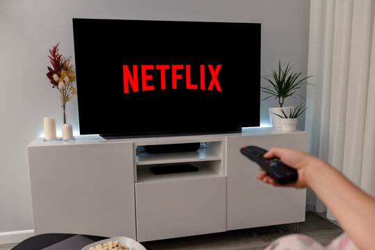 Woman watch the new online video streaming subscription netflix on TV. Holding remote controller. Netflix logo is on the screen