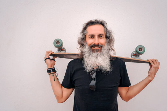 Portrait Happy Senior Or Mature Latino Man With Gray Beard Holding A Skateboard