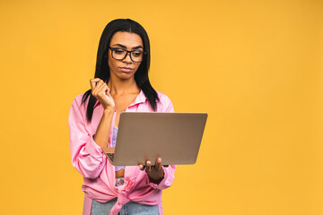 Young african american black positive serious cool lady using laptop and smiling isolated over yellow background.